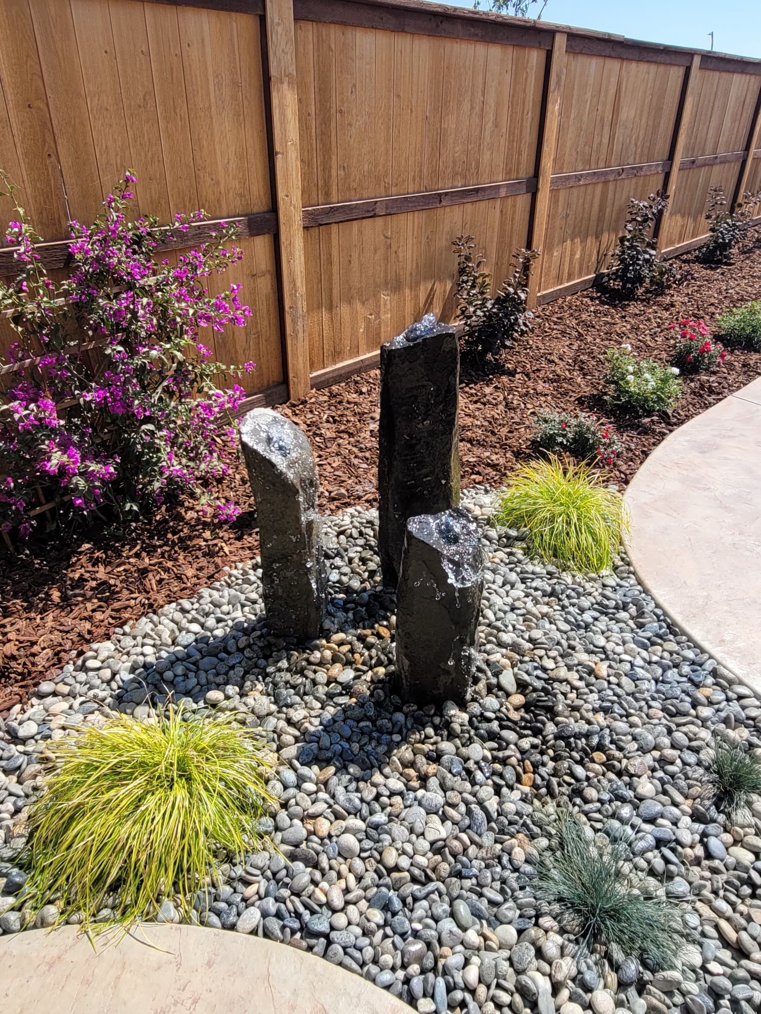 Basalt column fountain in river rock with bougainvillea and fresh planting beds