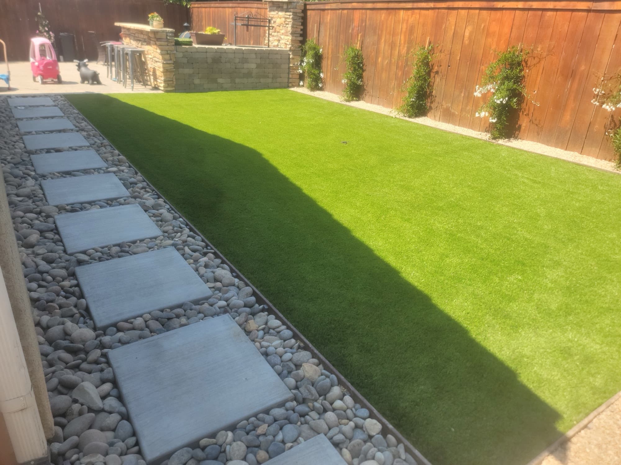 Backyard lawn with paver stepping stones, river rock, and a stone outdoor bar