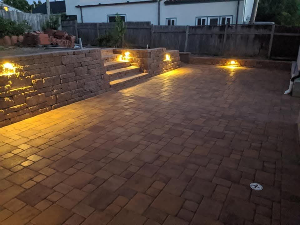 Paver patio and retaining wall with accent lighting at dusk