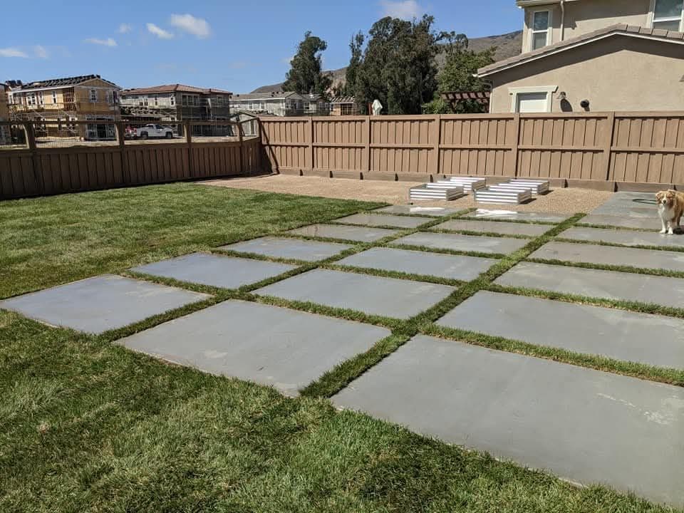 Large concrete pavers with grass strips in a fenced backyard